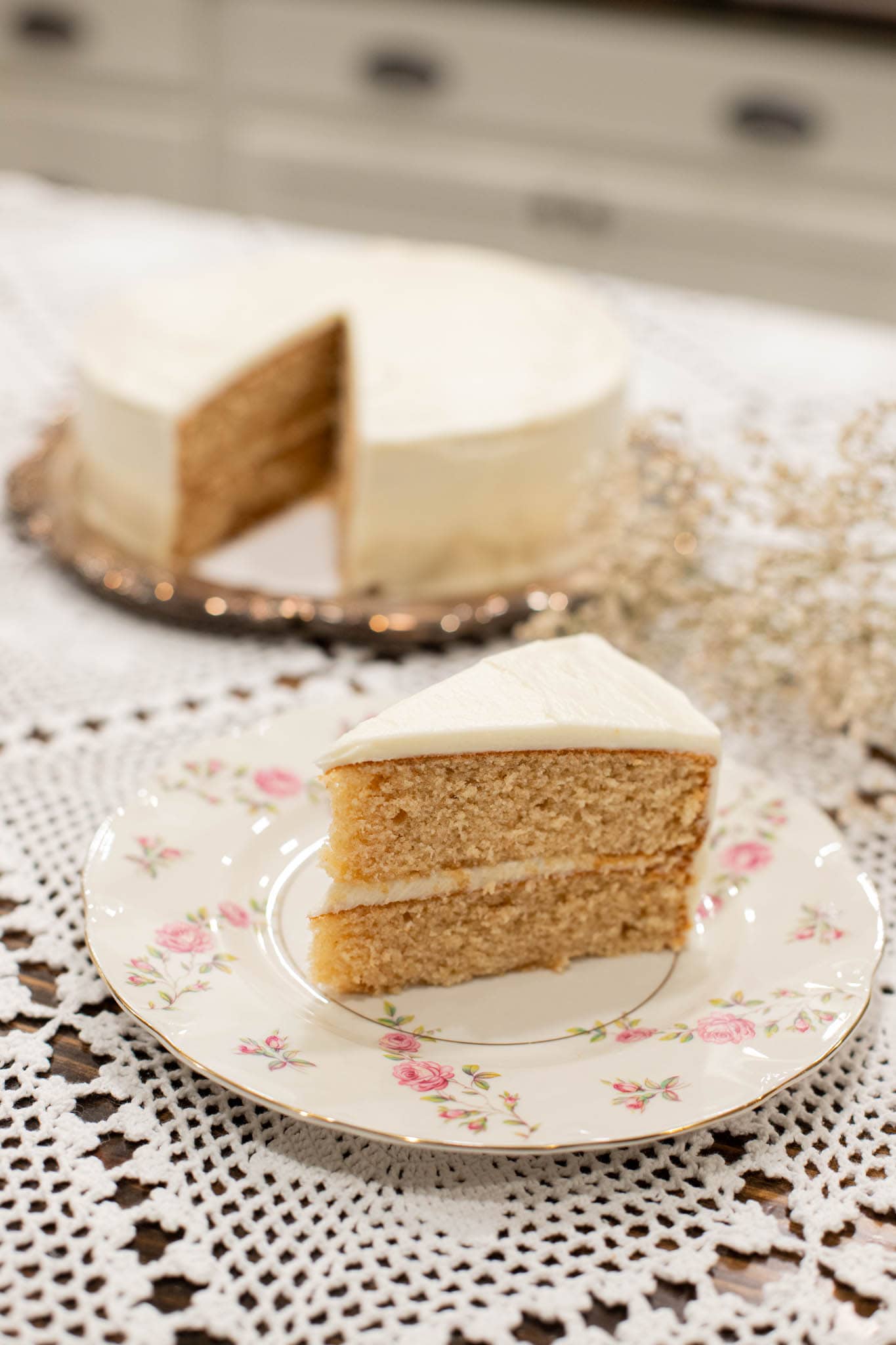 Slice of sourdough vanilla cake made with fresh milled flour on a floral vintage plate with white buttercream frosting and layered crumb visible.