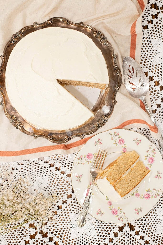 Overhead view of sourdough vanilla layer cake with fresh milled flour on a silver tray, frosted with smooth white buttercream and one slice removed.