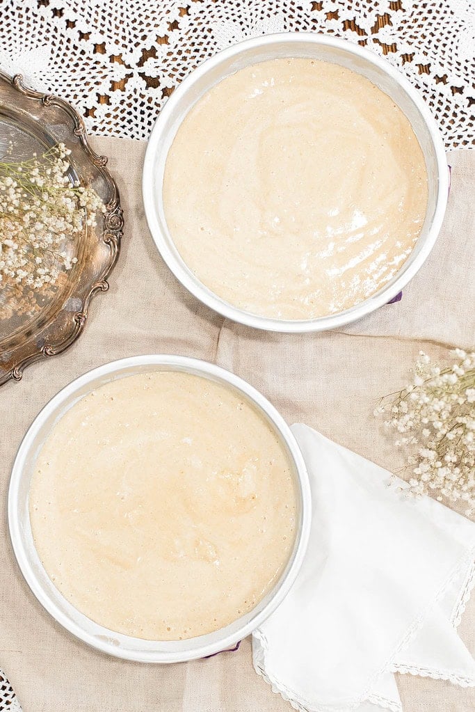 Two round cake pans filled with sourdough vanilla cake batter made from fresh milled flour, ready to bake on a linen-covered surface.