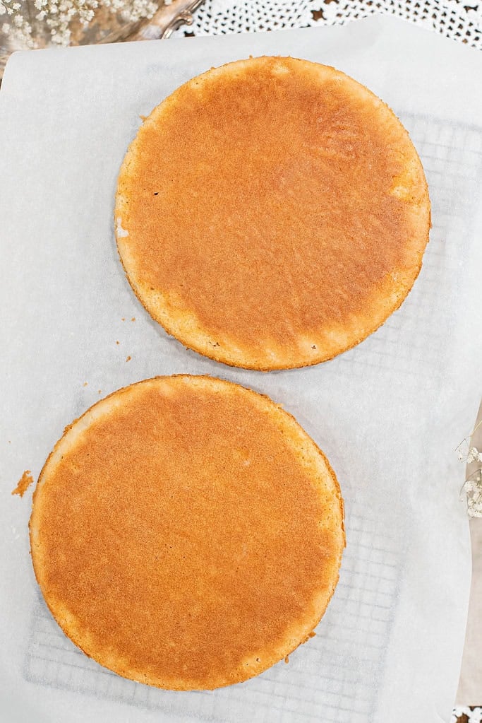 Two baked sourdough vanilla cake layers made with fresh milled flour cooling on parchment paper, golden brown tops visible.