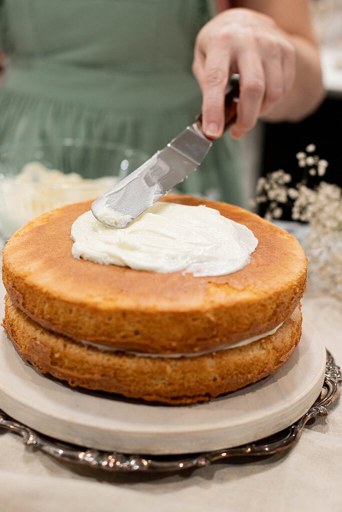 Spreading buttercream frosting onto a sourdough vanilla cake layer made with fresh milled flour using an offset spatula.