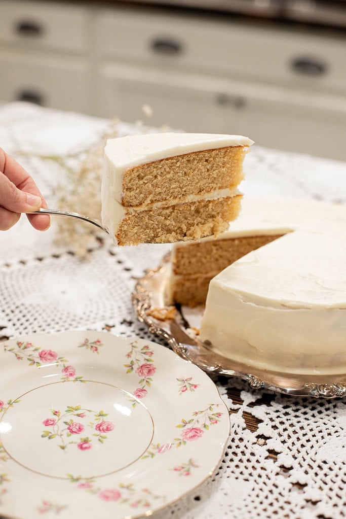 Slice of sourdough vanilla cake with fresh milled flour lifted on a cake server, showing tender crumb and smooth buttercream layers.