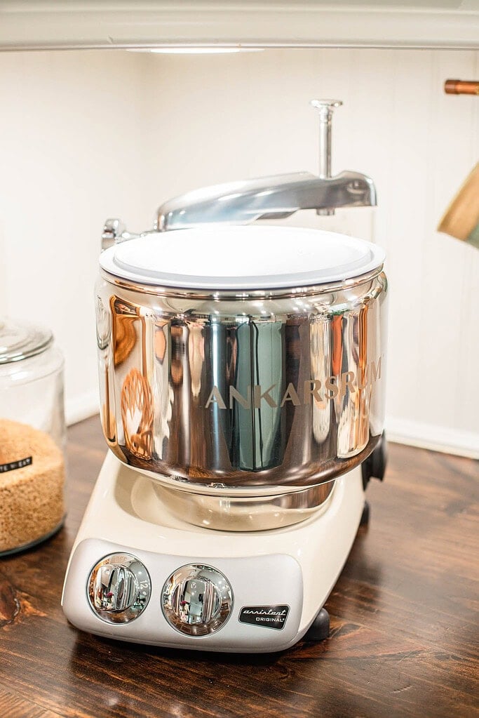 Ankarsrum stand mixer with stainless steel mixing bowl on a wooden counter, used for mixing dough made with freshly milled flour.