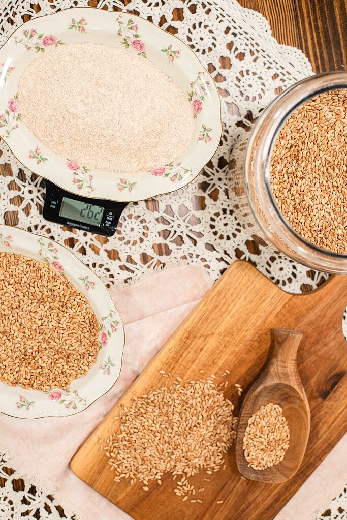 Whole wheat berries in a wooden bowl on top of a countertop grain mill with freshly milled flour nearby