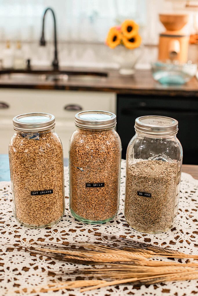 Oat groats, spelt, and rye in labeled mason jars on lace tablecloth in cottage kitchen