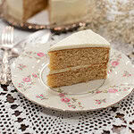 A beautifully plated slice of vanilla cake with buttercream frosting, with a blurred background of the remaining cake and delicate baby’s breath flowers.
