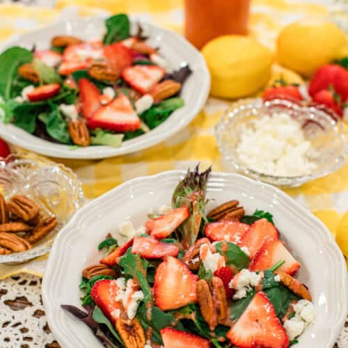 Close-up of a fresh strawberry and pecan salad with feta, spring mix, and strawberry vinaigrette. The image showcases texture and color with bright natural lighting and warm cottage kitchen vibes.