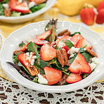 Strawberry spinach salad with pecans and feta cheese drizzled with strawberry vinaigrette in a white bowl.