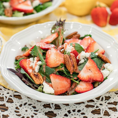 Strawberry spinach salad with pecans and feta cheese drizzled with strawberry vinaigrette in a white bowl.
