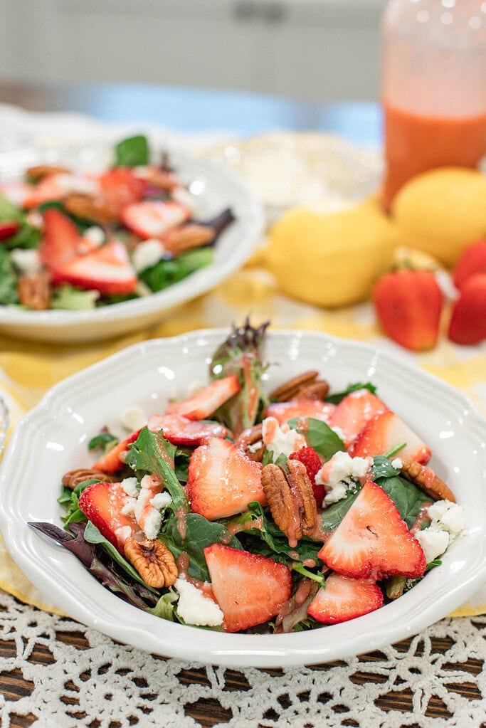 Strawberry spinach salad with pecans and feta cheese drizzled with strawberry vinaigrette in a white bowl.
