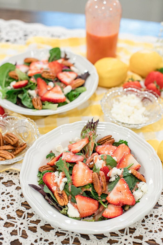 Two bowls of strawberry spinach salad topped with sliced strawberries, pecans, feta cheese, and strawberry vinaigrette dressing.