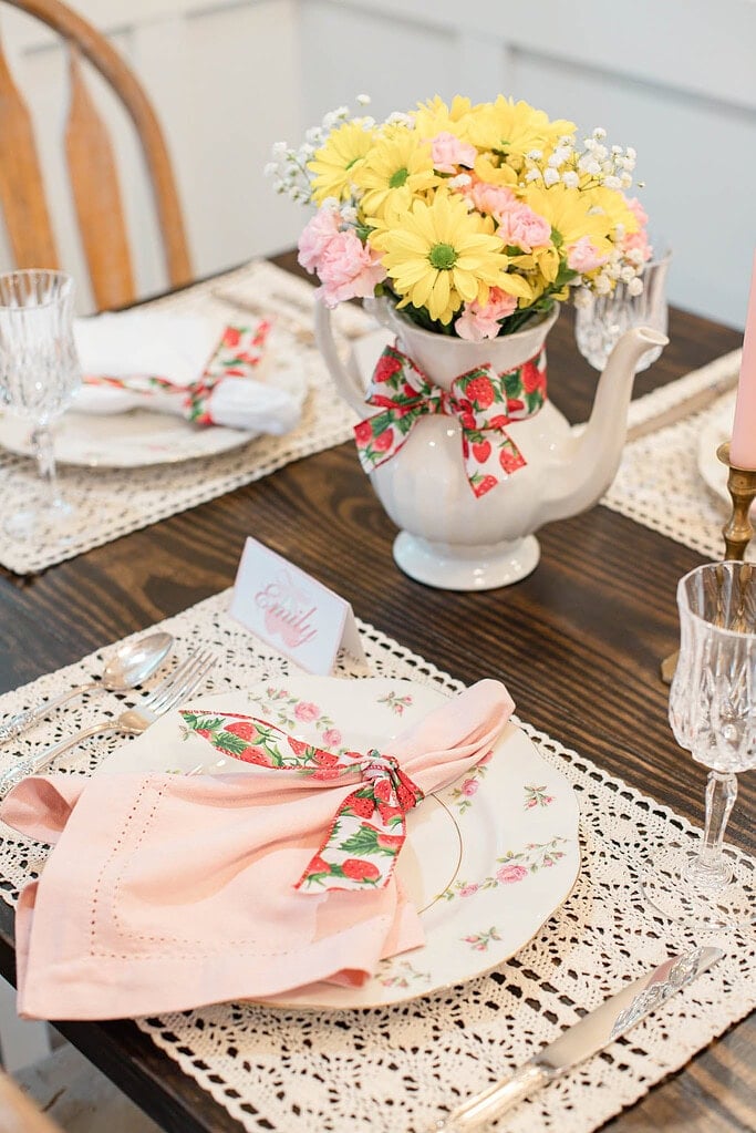 Strawberry tablescape place setting with floral plate, pink napkin, and ribbon on lace placemat