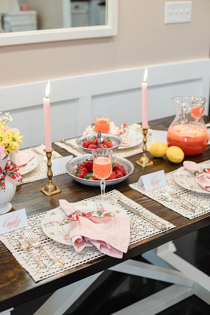 Strawberry tablescape with lemonade pitcher, lemons, tiered tray, and pink candles on dining table