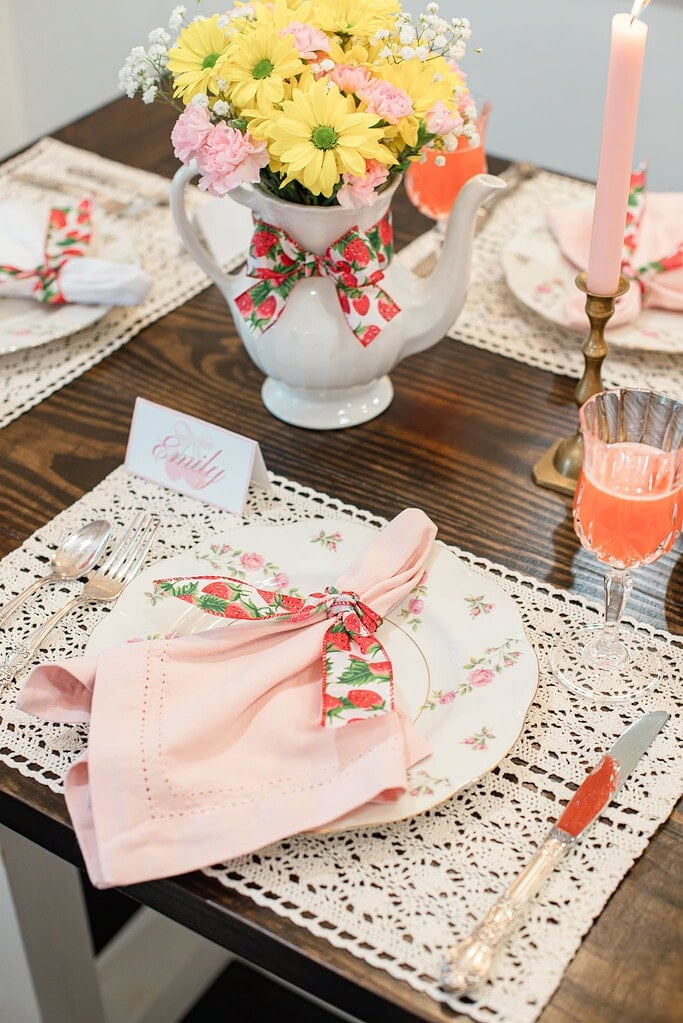 Strawberry ribbon napkin on floral plate with name card and glassware on lace placemat
