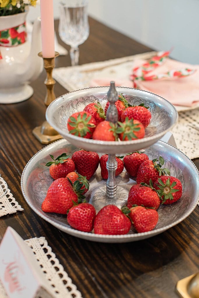 Strawberries arranged on tiered metal tray on cottage dining table with candlelight