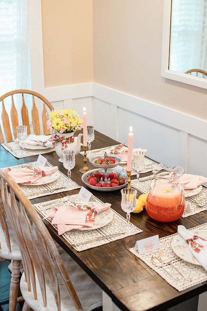 Strawberry cottage tablescape with lemonade pitcher, candles, tiered tray, and floral place settings
