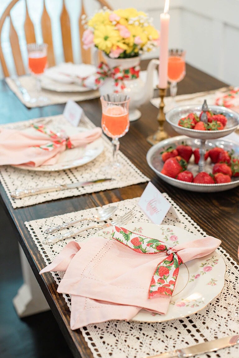 Strawberry ribbon napkin folded on floral plate with lace placemat and glassware on dining table