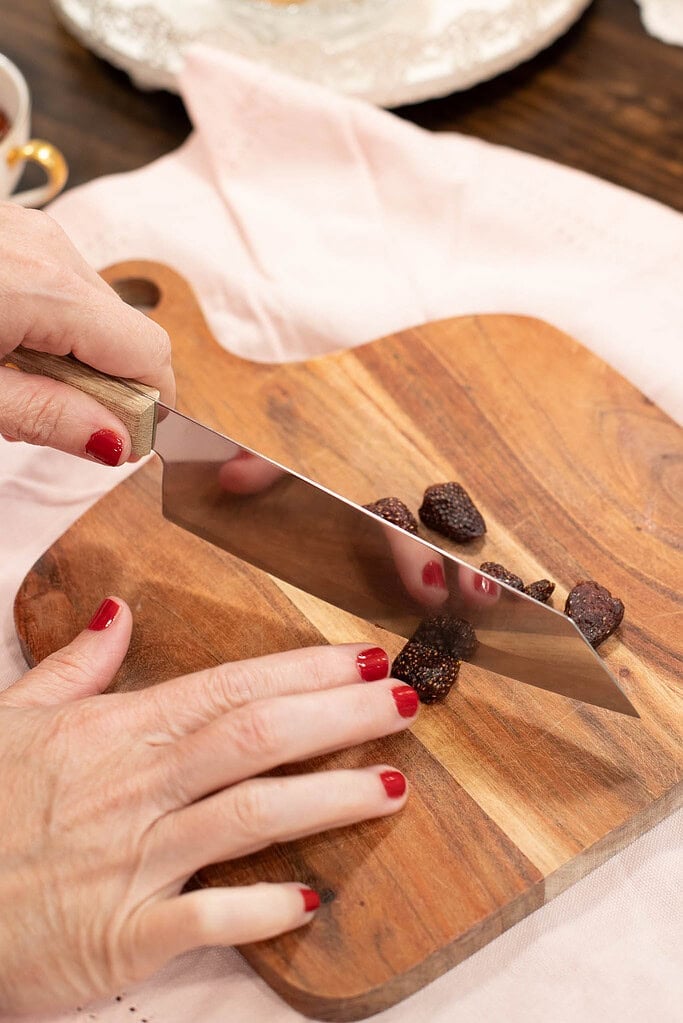 Hands slicing dried strawberries on wooden cutting board for homemade strawberry tea recipe