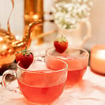 Two clear glass cups filled with strawberry tea garnished with fresh strawberries on cozy tea table