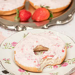Strawberry cream cheese spread generously over a bagel on a floral plate with fresh strawberries in the background.
