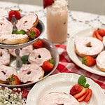 Bagels generously topped with whipped strawberry cream cheese served on white plates and a tiered tray, garnished with fresh strawberries and mint leaves.