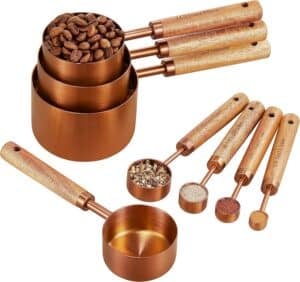 Copper measuring cups and spoons with wooden handles, displayed with coffee beans and spices, ideal for accurate and beautiful baking prep.