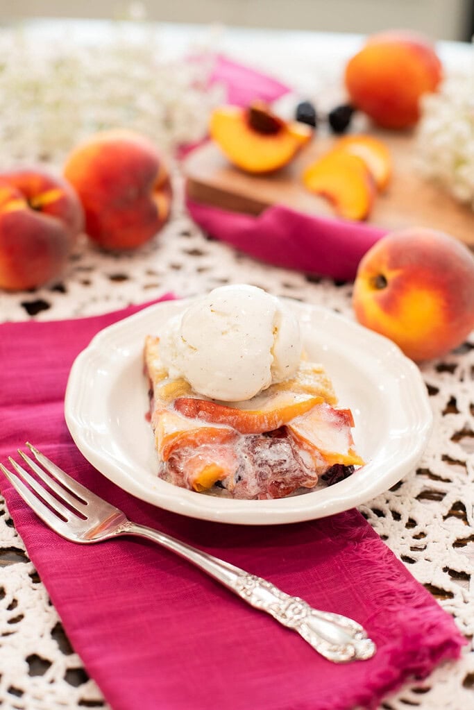 Slice of sourdough peach blackberry galette with vanilla ice cream served on white plate