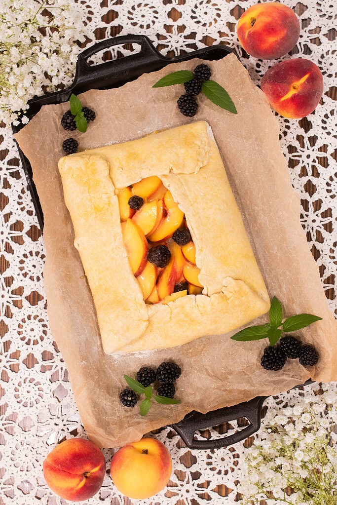Rustic sourdough peach blackberry galette with folded crust on parchment lined pan