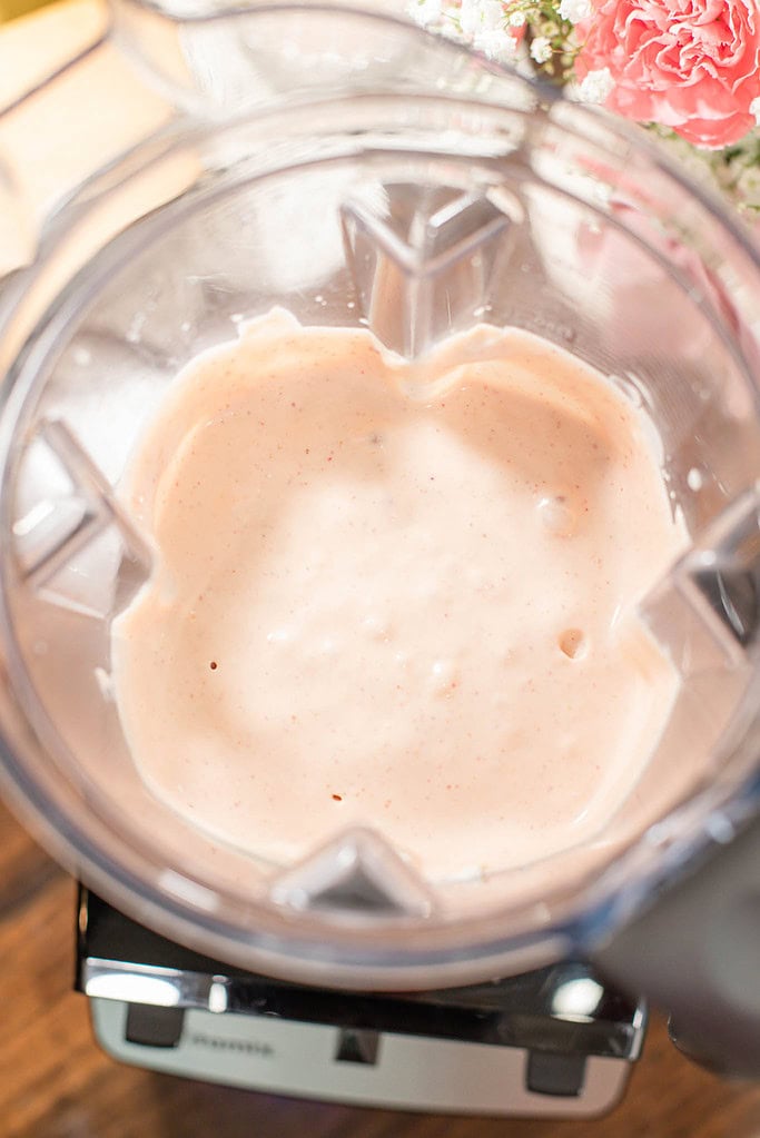 Smooth strawberry cheesecake mixture blended inside a blender viewed from above.