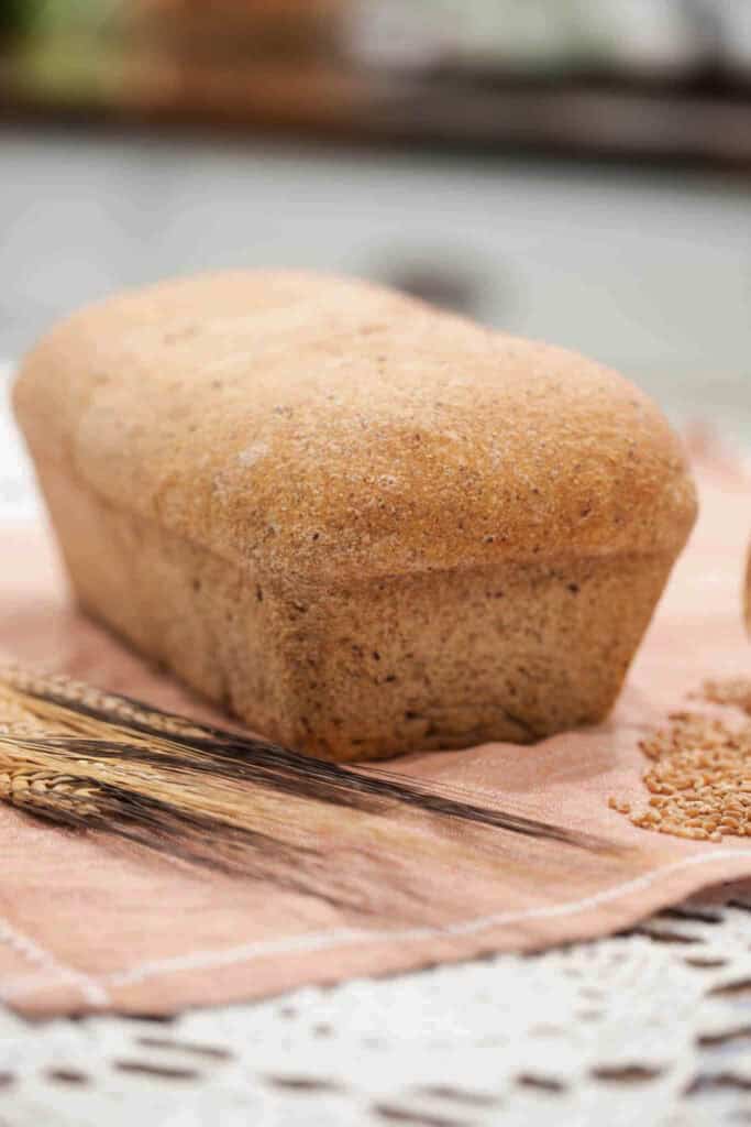Whole wheat sandwich loaf made with freshly milled flour, resting on a pink linen with wheat stalks nearby.