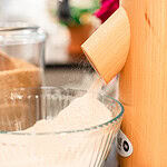 A wooden flour mill pouring flour into a large bowl.
