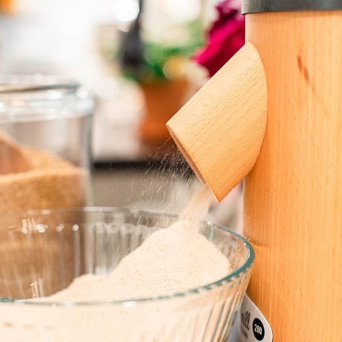 A wooden flour mill pouring flour into a large bowl.