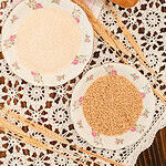 Two floral plates with flour and wheat berries on a lace cloth.