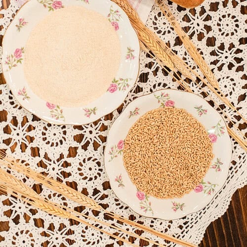 Two floral plates with flour and wheat berries on a lace cloth.