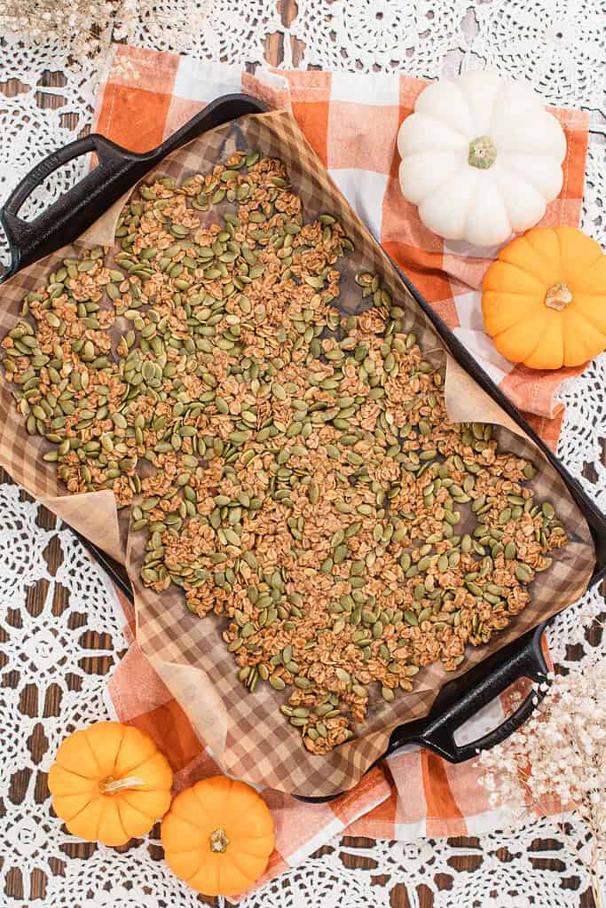 Overhead view of a full baking sheet of pumpkin seed brittle, surrounded by mini pumpkins, dried flowers, and a checkered cloth.