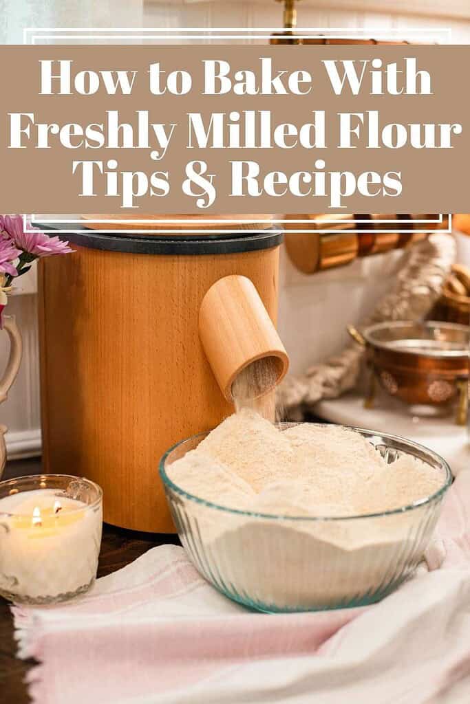 Freshly milled flour pouring from a wooden grain mill into a glass bowl on a cozy cottage countertop surrounded by candles and kitchen linens.”