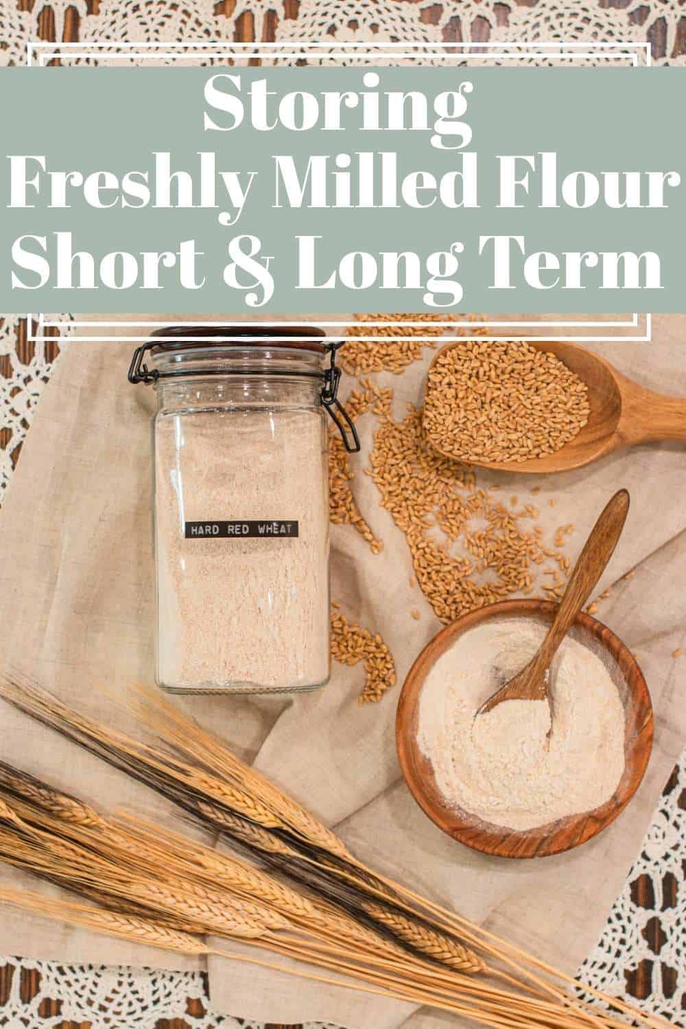 Glass jar labeled hard red wheat filled with freshly milled flour beside a wooden bowl, scoop, and dried wheat stalks, showing how to store flour short and long term in a cozy kitchen