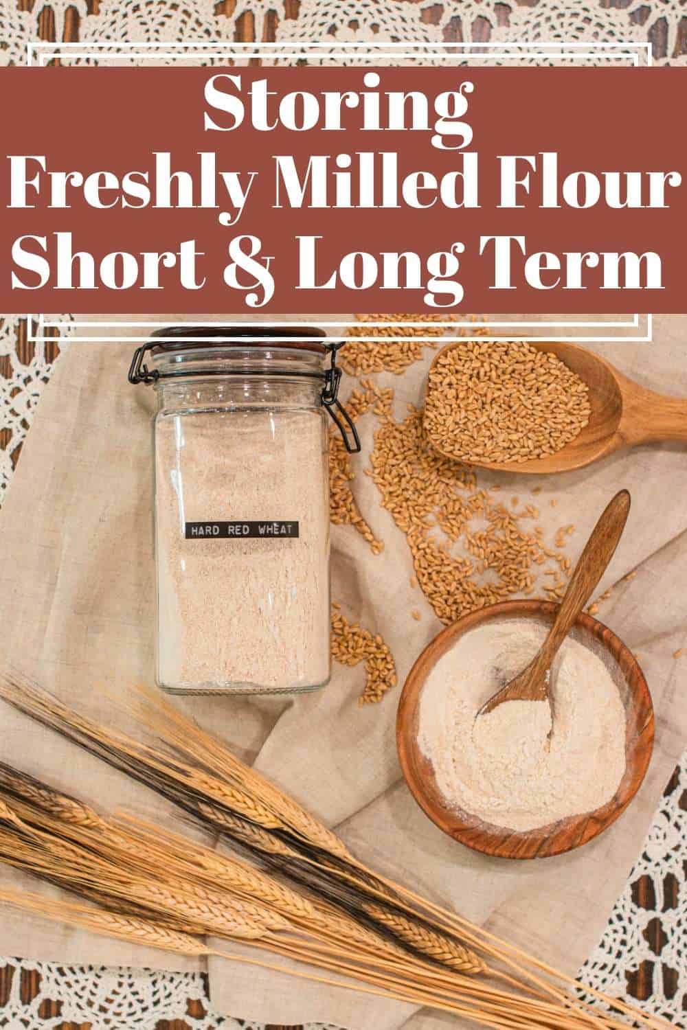 A labeled jar of hard red wheat flour sits beside a wooden bowl of freshly milled flour, a wooden scoop of wheat berries, and dried wheat stalks on linen over vintage lace. Text overlay reads “Storing Freshly Milled Flour Short & Long Term,” illustrating how to properly store home-milled flour for both short- and long-term use in a cozy cottage kitchen setting.