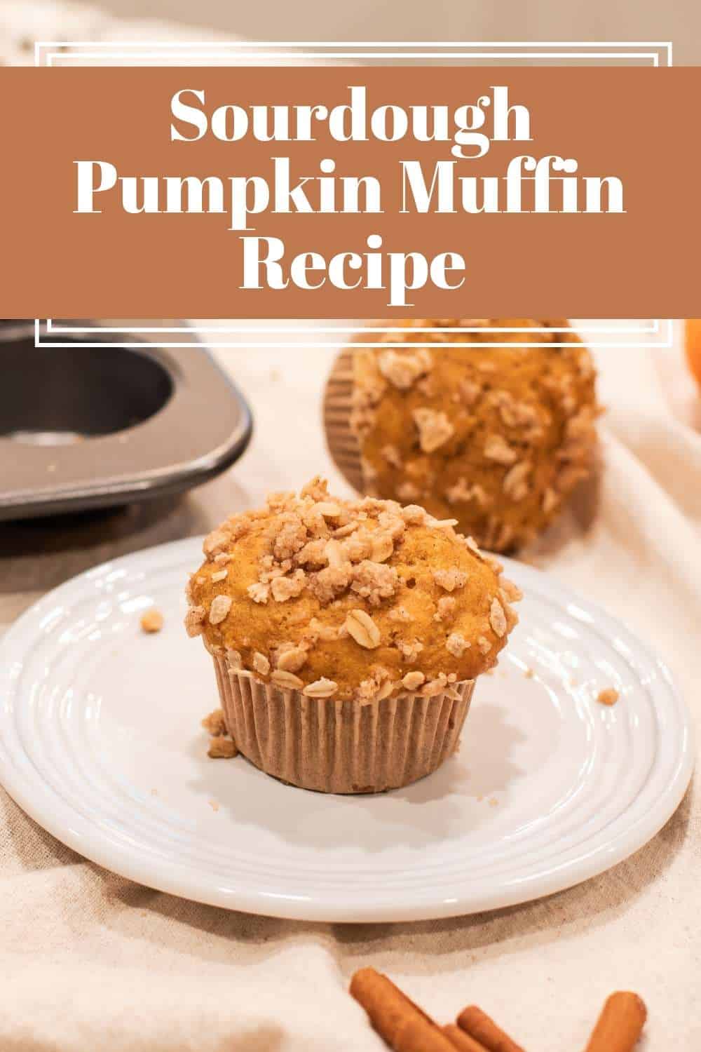Golden sourdough pumpkin muffin topped with a crunchy oat streusel, served on a white plate with a muffin tin and warm autumn spices in the background. Text overlay reads: Sourdough Pumpkin Muffin Recipe.