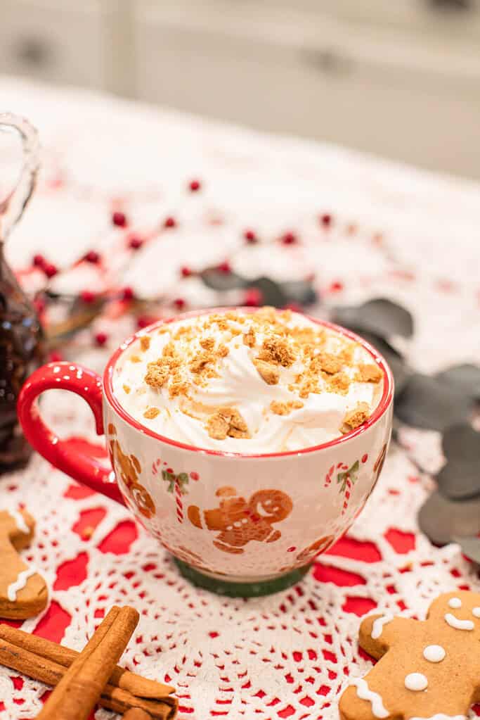 gingerbread latte in a festive mug, topped with whipped cream and crushed cookie crumbs.