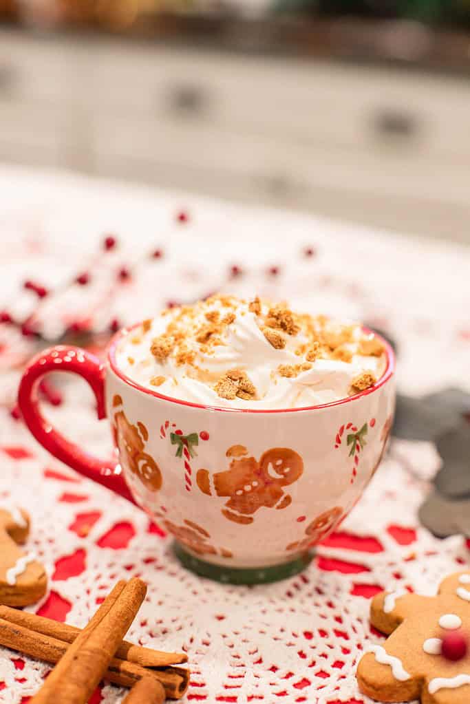 A gingerbread latte in a red-handled mug decorated with gingerbread figures, topped with whipped cream and crumbs.
