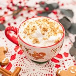 Close-up of a gingerbread latte topped with whipped cream and gingerbread cookie crumbs on a holiday table.