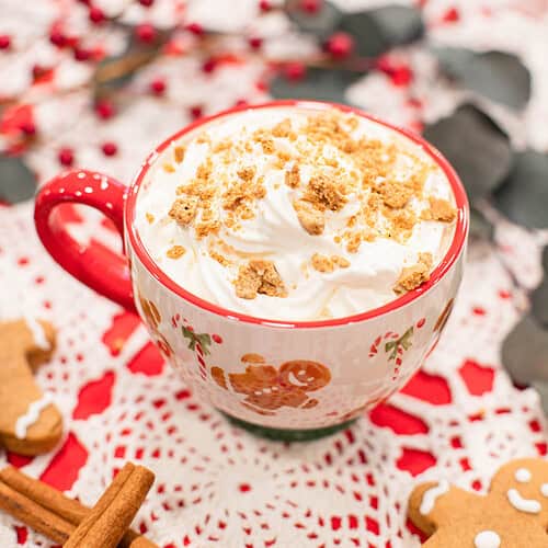 Close-up of a gingerbread latte topped with whipped cream and gingerbread cookie crumbs on a holiday table.