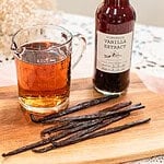 Vanilla beans on a wooden board next to a measuring cup of alcohol and a bottle of homemade vanilla extract.