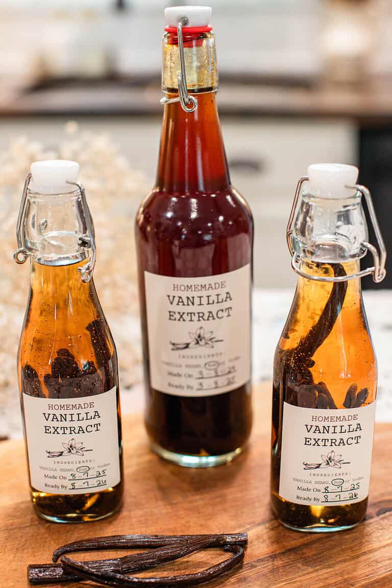 Three swing-top bottles filled with homemade vanilla extract and whole vanilla beans.