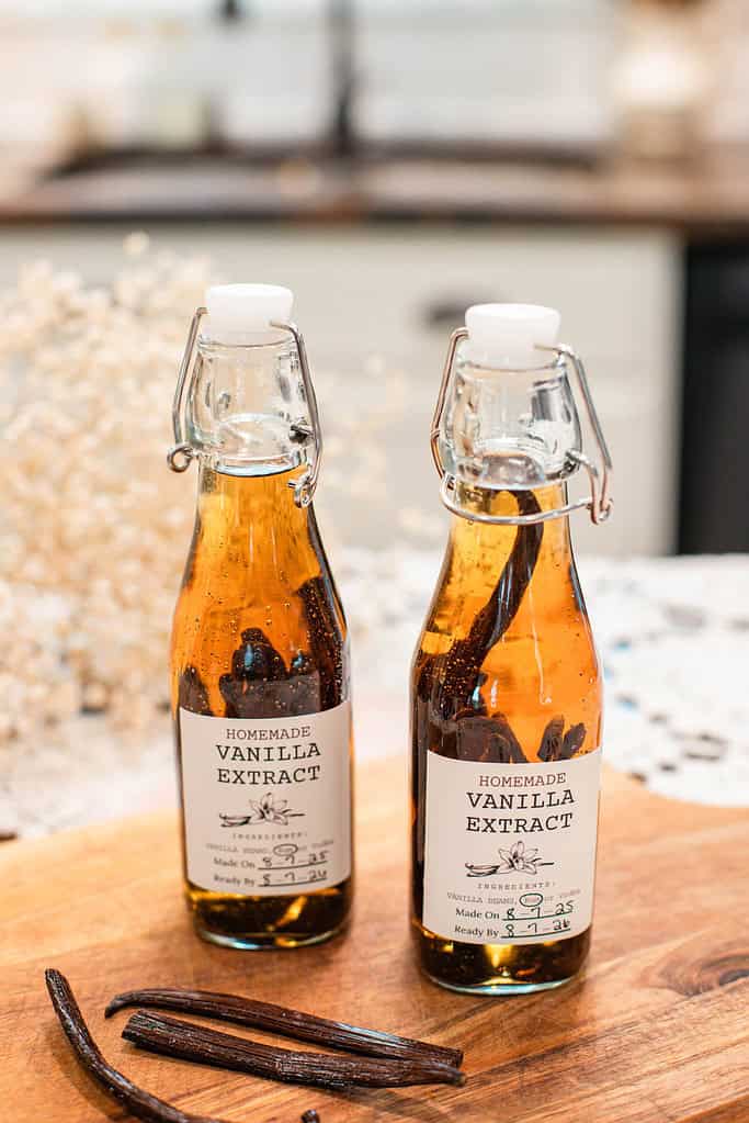 Two bottles of homemade vanilla extract sitting on a wooden board with vanilla beans in front.