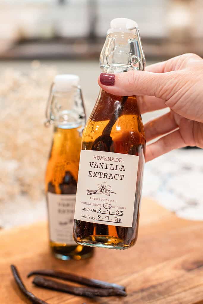 A hand holding a small bottle of homemade vanilla extract with whole vanilla beans inside.