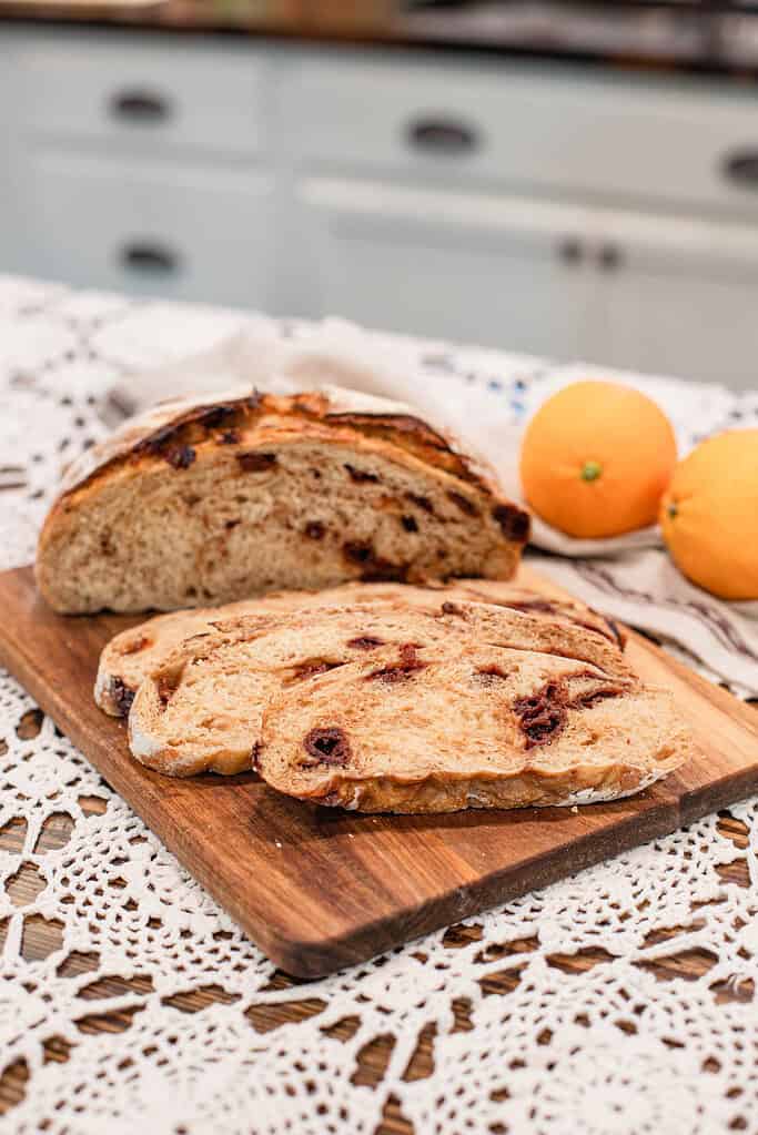 Sliced sourdough cranberry orange bread on a wooden board, showing soft, airy crumb speckled with cranberries.