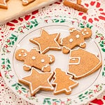 A close shot of the holly plate filled with gingerbread cookies in different holiday shapes. The texture of the cookies shows soft crumb and smooth edges, and the white icing outlines add a simple, classic finish.