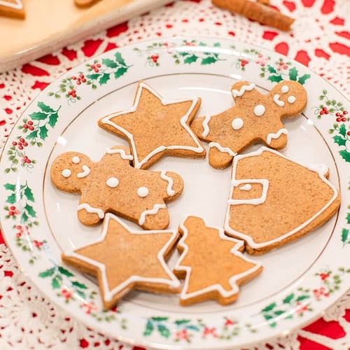 A close shot of the holly plate filled with gingerbread cookies in different holiday shapes. The texture of the cookies shows soft crumb and smooth edges, and the white icing outlines add a simple, classic finish.